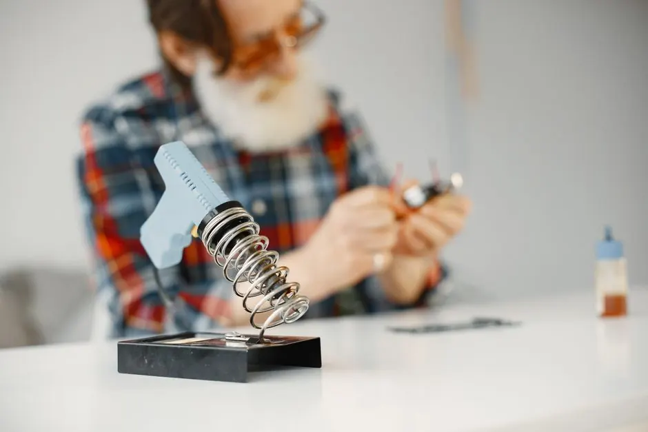 A soldering iron and man working on electronic component at a desk indoors.