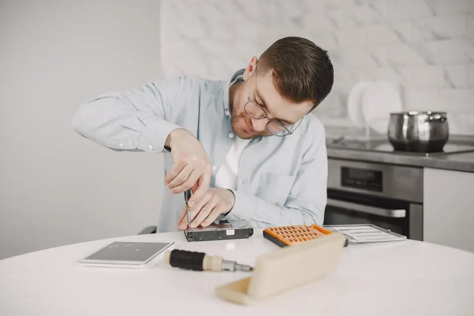 Man wearing glasses using a screwdriver to fix a device on a kitchen table.